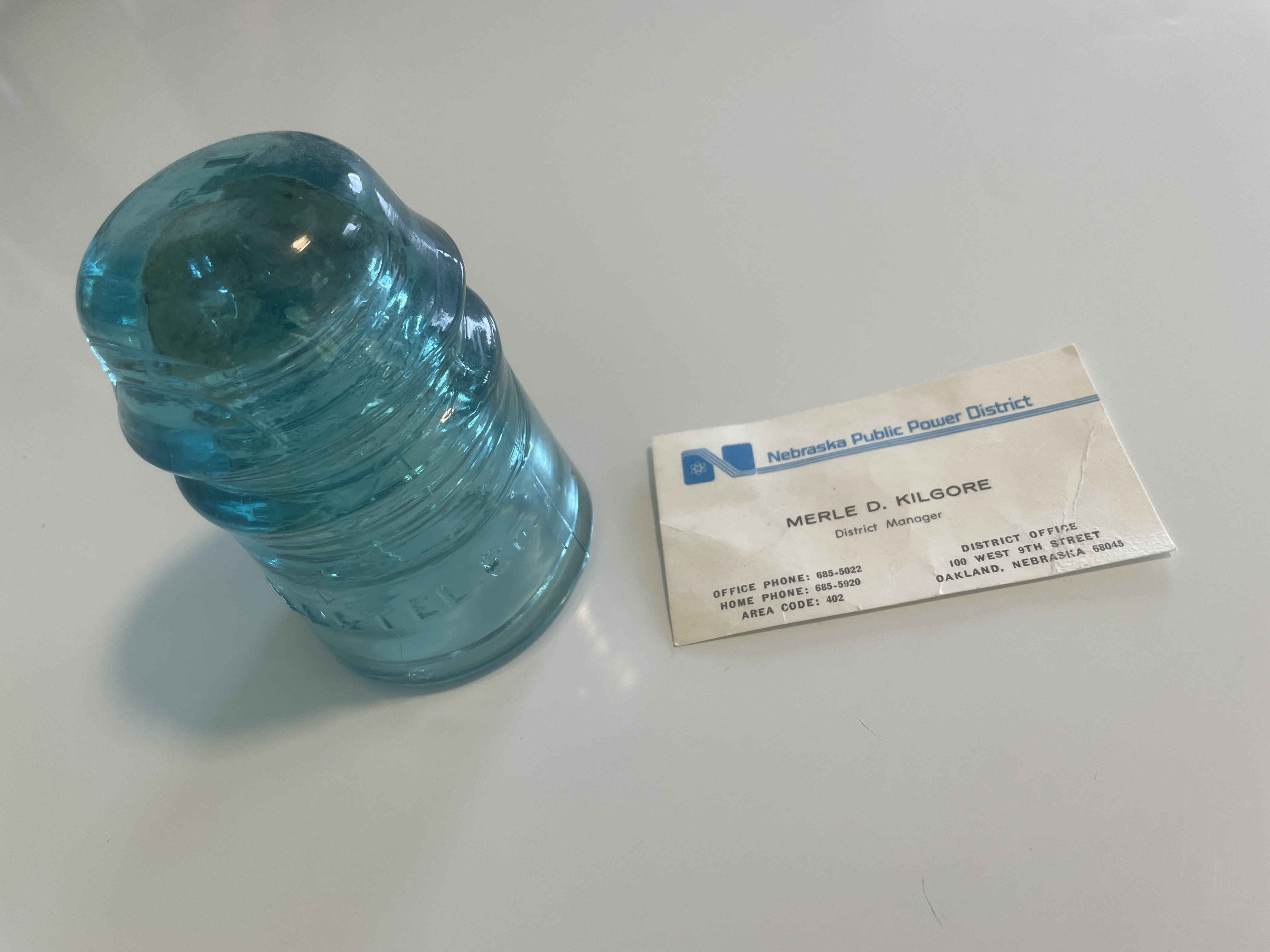 A blue glass insulator next to a business card of Merle D. Kilgore, District Manager, Nebraska Public Power District
